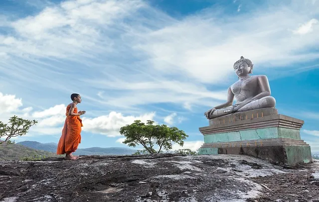 A young monk in front of a seated Buddha statue