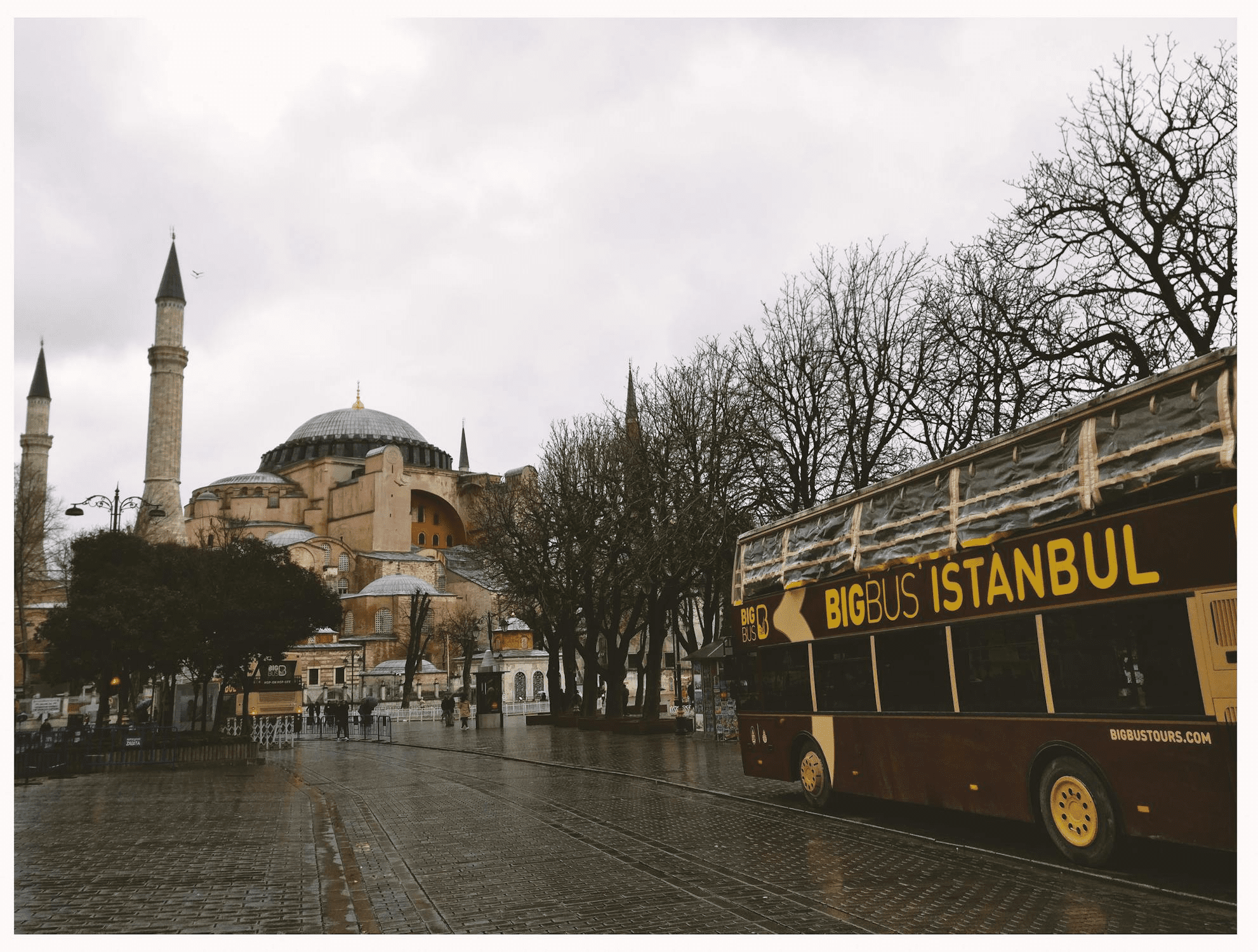 Hagia Sophia mosque with minarets on rainy day with tourist bus labeled "BIGBUS ISTANBUL" in foreground.
